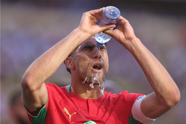 A Morocco player pours water over his head on the field, with water streaming down his face and red jersey.