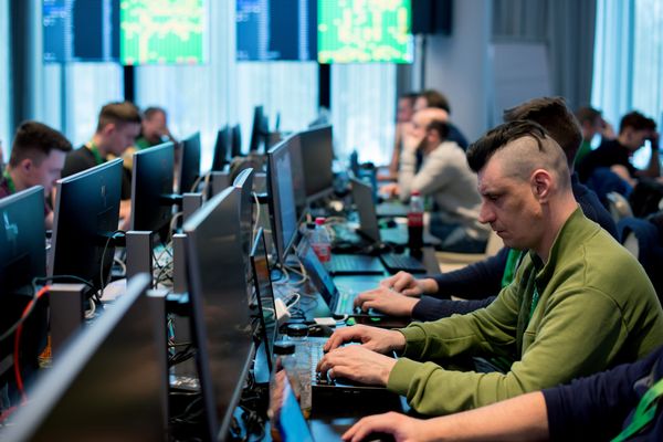 Rows of cybersecurity specialists work at computer stations in a crowded operations room.