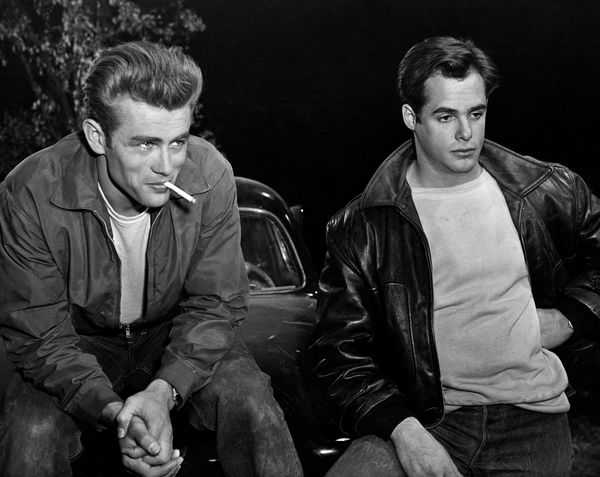 Actor James Dean smokes a cigarette beside another actor in a scene from Rebel without a Cause.