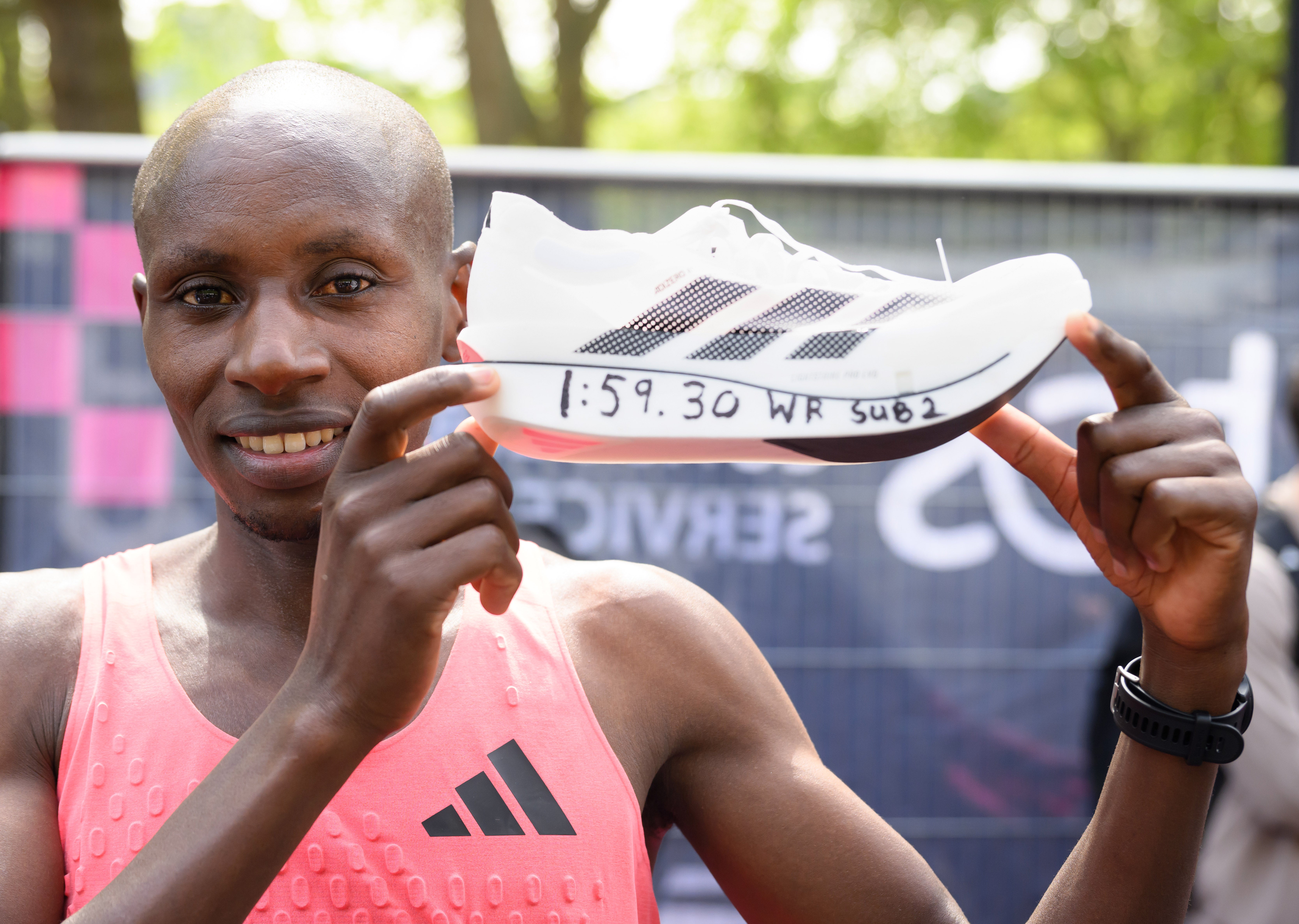 Sabastian Sawe in a pink Adidas top holding up his Adidas running shoes after winning the London Marathon.