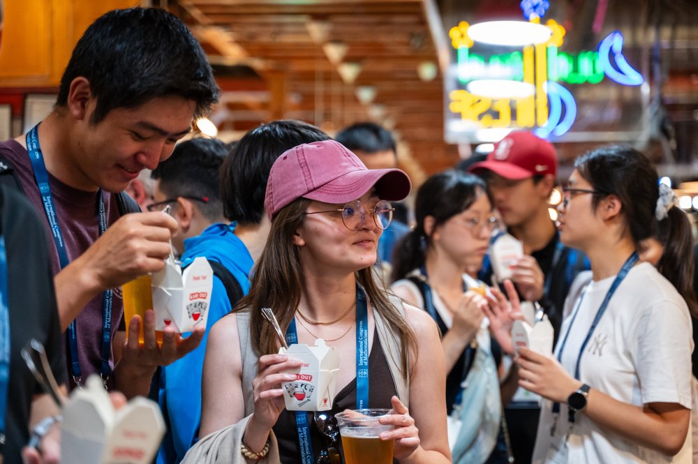 Young mathematicians hold beers and takeout containers as they smile and stand in circles.
