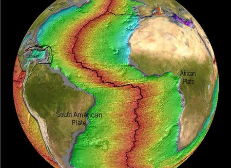 A colorized view of part of the globe of Earth showing South American, Africa and parts or North America and Europe. A jagged red line runs down the Atlantic Ocean basin showing where a mid-ocean ridge is