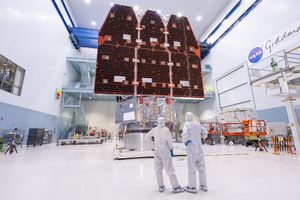 Two bunnysuited engineers stand facing away from the camera in a large clean room at NASA's Goddard Space Flight Center, gazing at flight hardware for the space agency's Nancy Grace Roman Space Telescope.