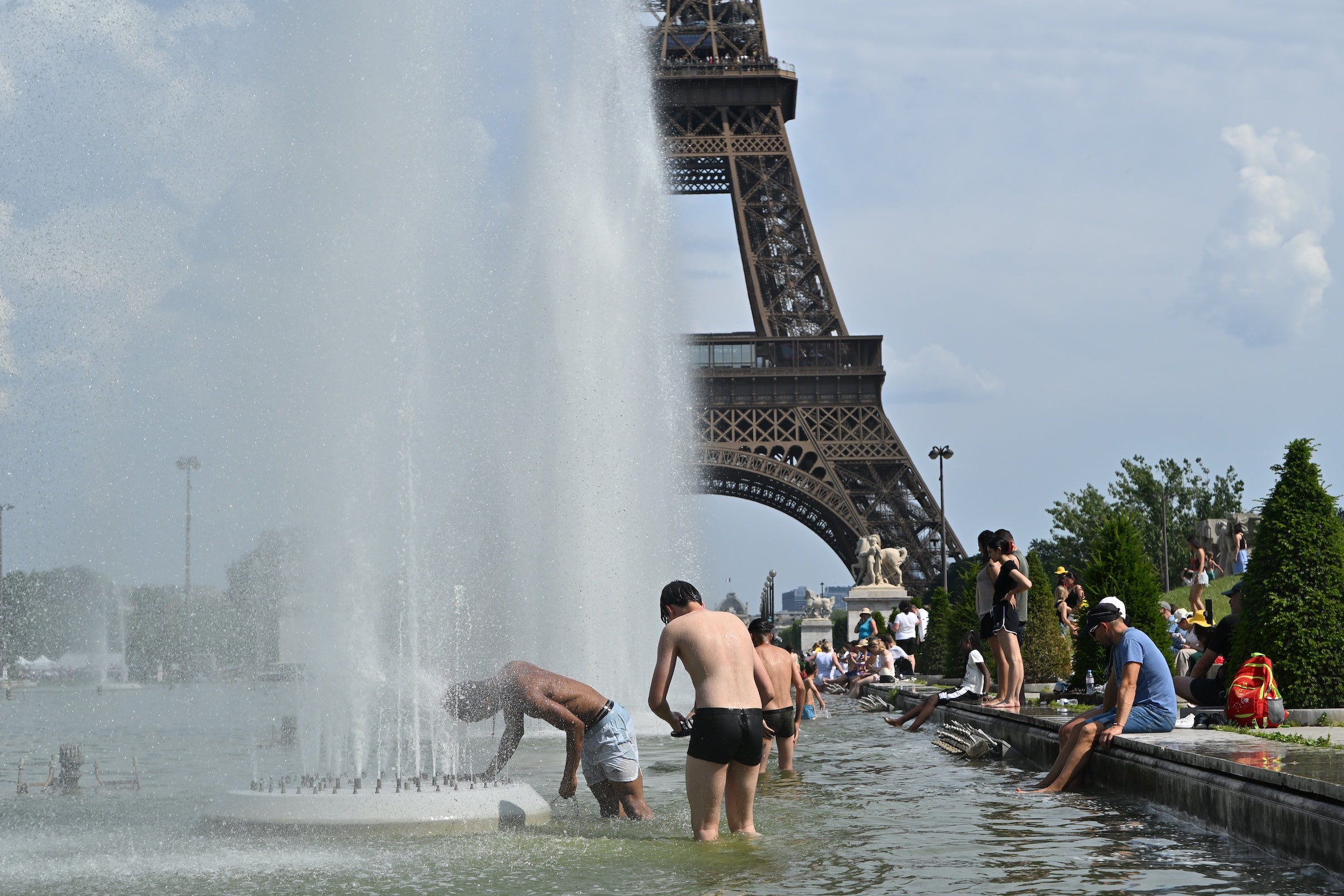 People in bathing suits stand in a large knee-high pool with fountains and the Eiffel Tower in the background.