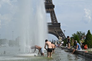People in bathing suits stand in a large knee-high pool with fountains and the Eiffel Tower in the background.