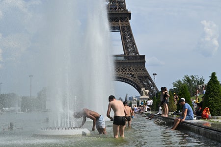 People in bathing suits stand in a large knee-high pool with fountains and the Eiffel Tower in the background.