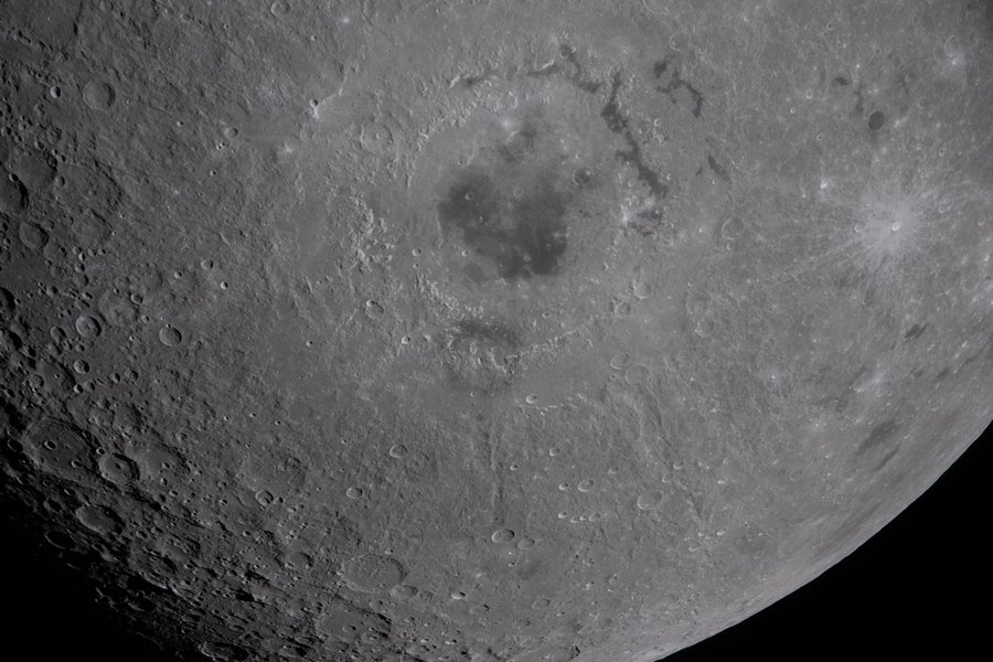 A close-up photograph of the moon with a large basin visible in the center.