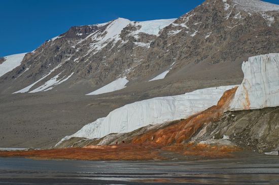 A brown, snow-capped landscape with a bright orange red fall going into the water