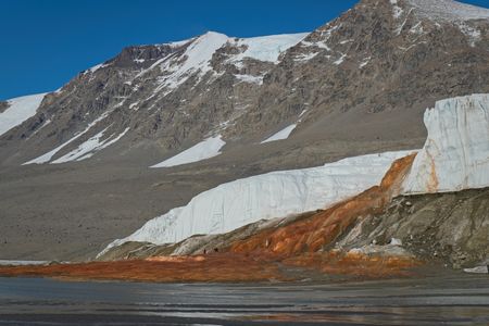 A brown, snow-capped landscape with a bright orange red fall going into the water