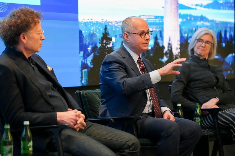 Two men and one woman dressed in business formal talking on a panel.