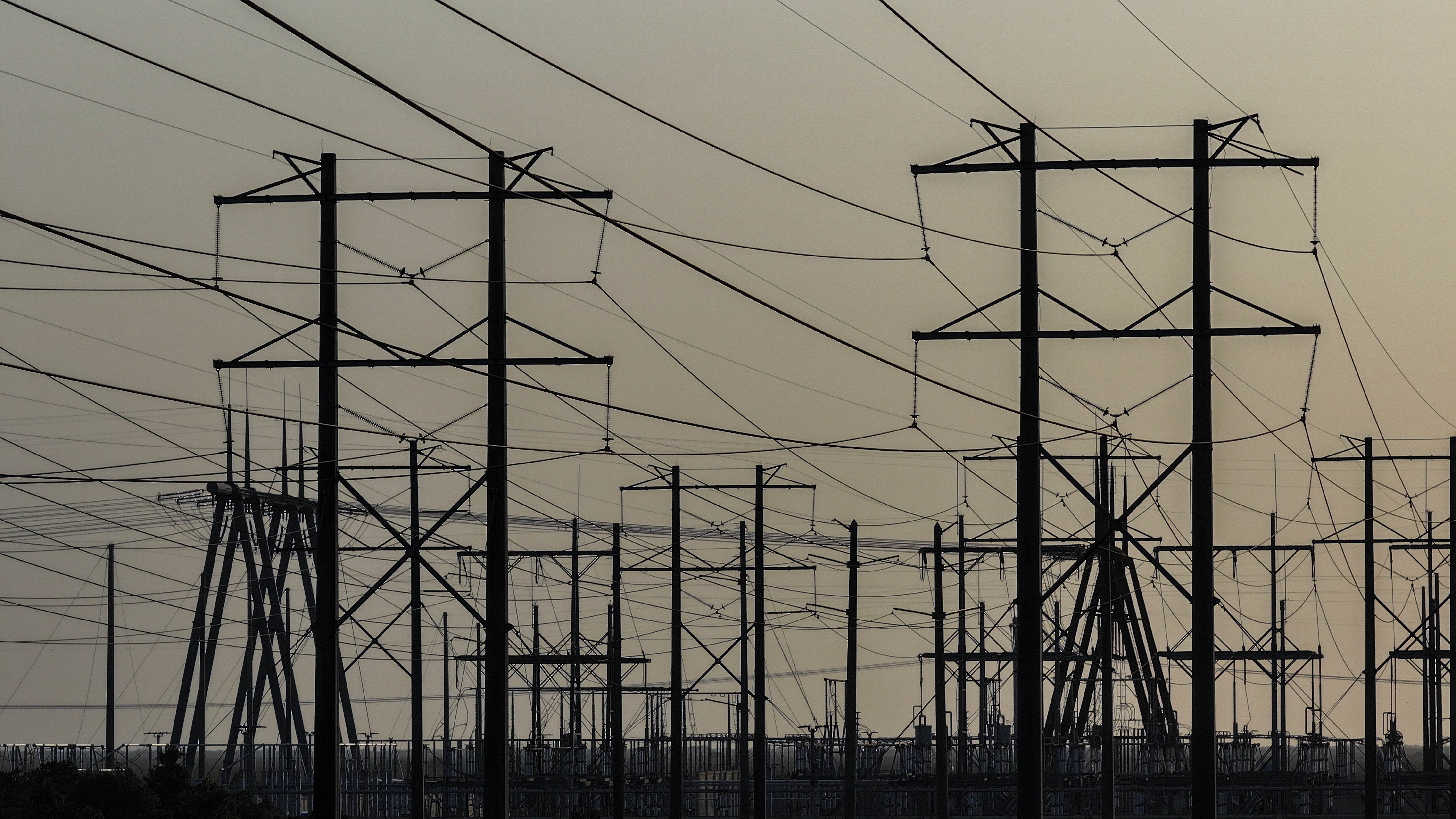 Power lines and electricity transmission towers against a sunset or sunrise