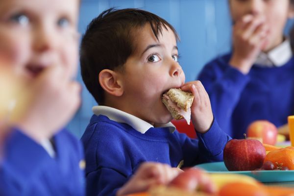 Child in blue school uniform eating a sandwich at a school lunch table