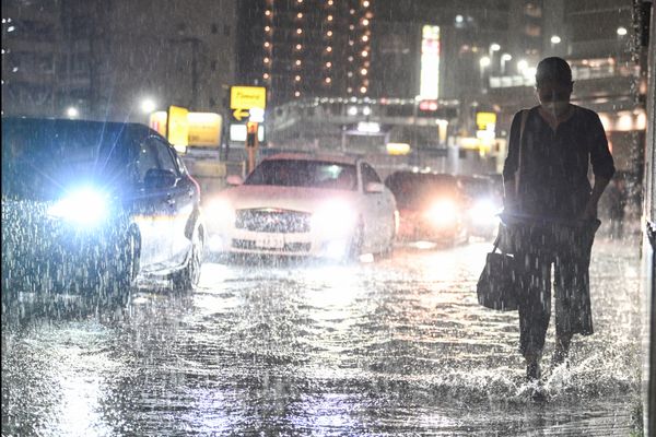 A figure walking in the rain as cars pass.