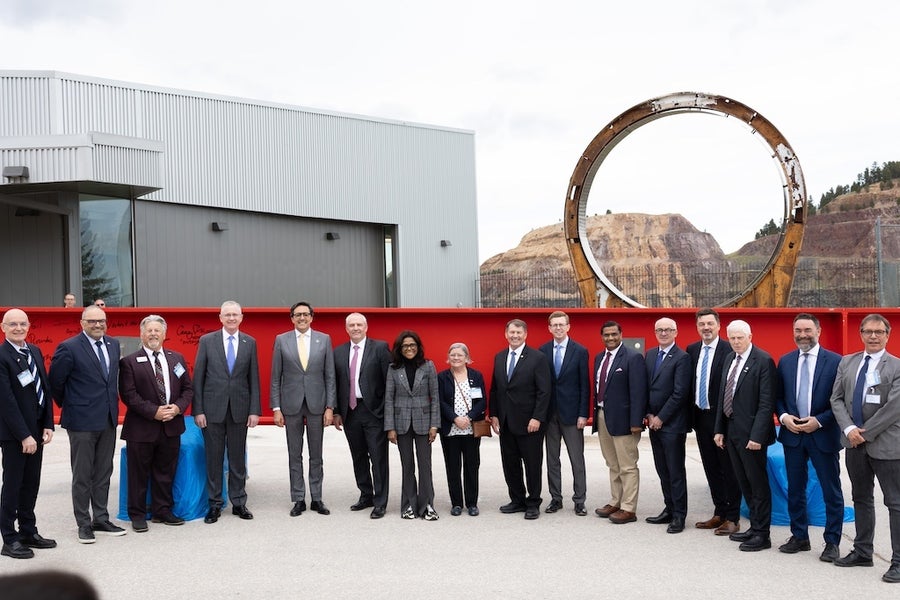 Suited officials guidelines successful a statement successful beforehand of a elephantine reddish alloy beam, against a backdrop of brownish mountains.