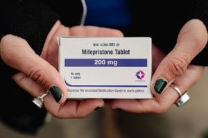 A pair of hands with painted nails and rings on holds a box of mifepristone.