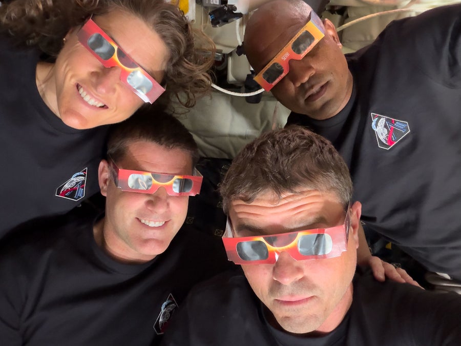 Four people wearing eclipse glasses inside a space capsule.