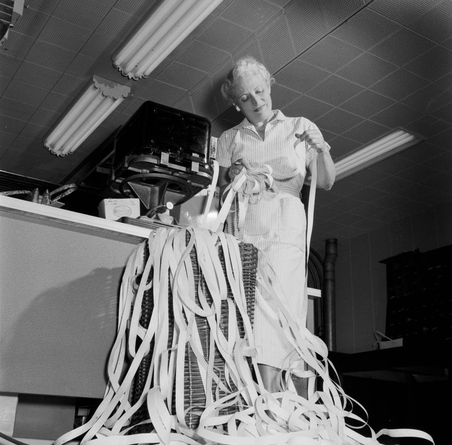 Black-and-white image of ticker tape collecting at a desk.