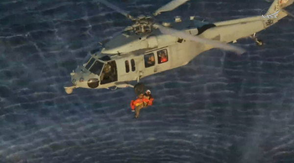 NASA astronaut Reid Wiseman is seen midair being hoisted into a helicopter above the Pacific Ocean.