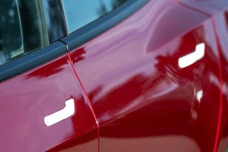 Two flush door handles on the side of a red Tesla Model 3.