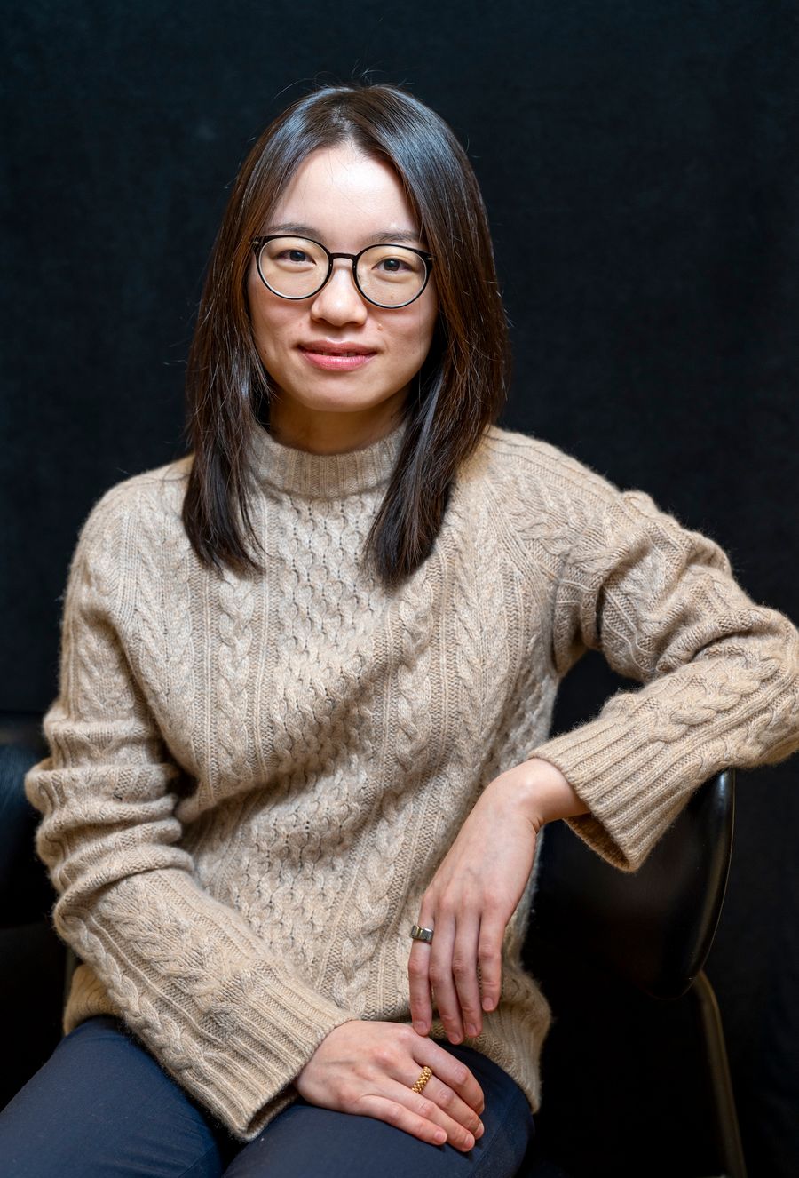 A female successful glasses poses casually against a acheronian background