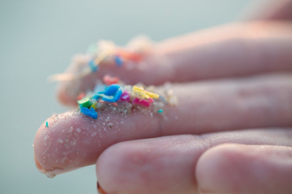 Fingers with small colorful particles of plastic stuck to them.