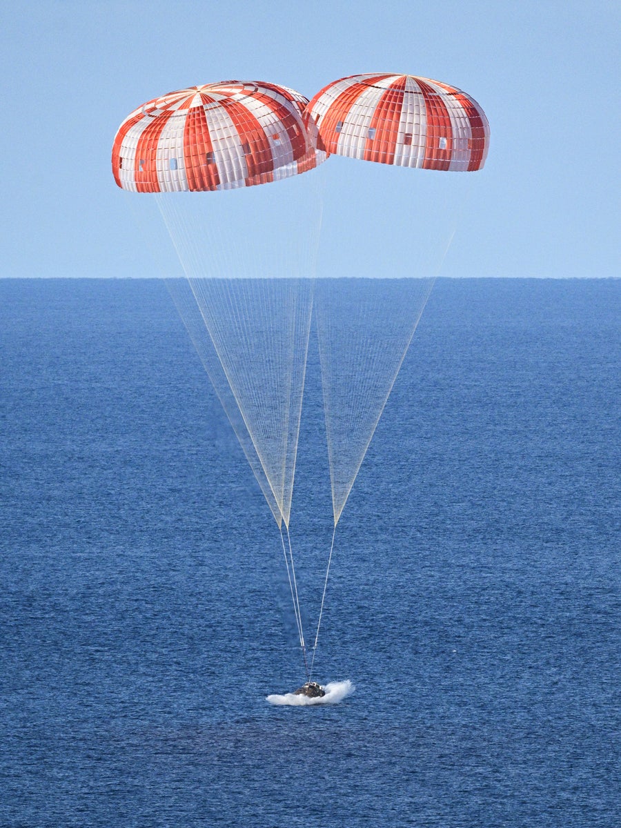 A tiny spacecraft with two large parachutes above lands on a blue Pacific Ocean.