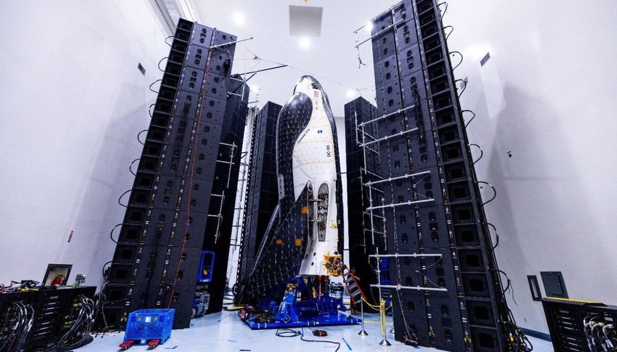 A space plane sits vertically in a large testing chamber.