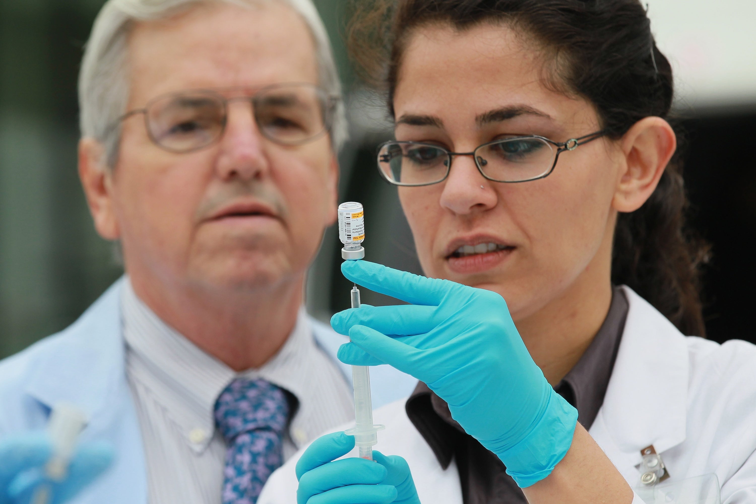 A woman on the right draws an injection into a needle as a man behind her observes on the left.