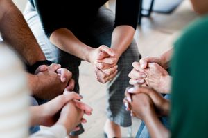 Five people sit in a circle in chairs, tight focus on their hands.