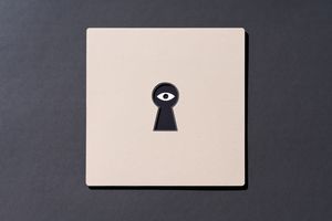 An eye on the other side of a keyhole cut out of paper