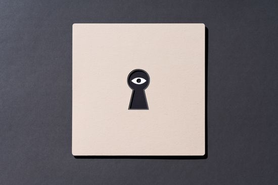 An eye on the other side of a keyhole cut out of paper