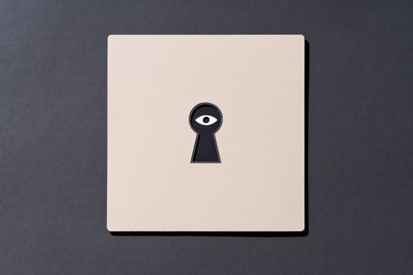 An eye on the other side of a keyhole cut out of paper