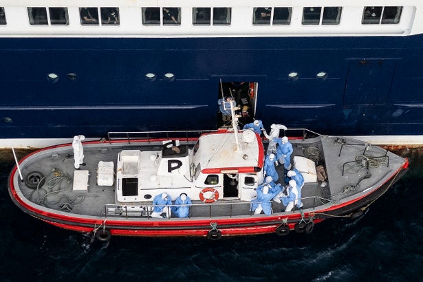 This aerial view shows health personnel assisting patients onto a boat from the cruise ship MV Hondius. Medics in blue suits can be seen guiding passengers off the ship onto a smaller boat for evacuation.
