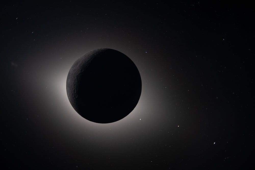 La luna aparece como una esfera oscura, con una tenue luz blanca visible detrás de ella.