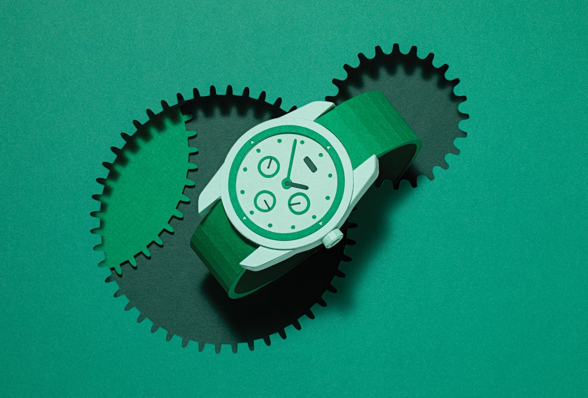 A dimensional watch inside a cutout of a toothed gear against a green background.