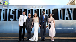 The director and cast of the movie Disclosure Day pose in front of a banner with the name of the movie for a promotional event