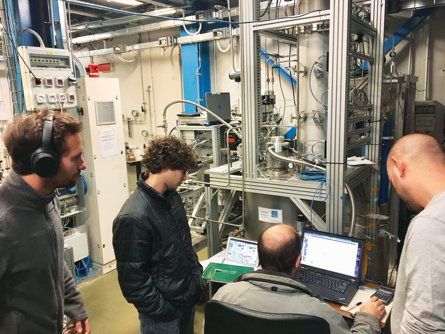 The author, now wearing street clothes, and two other men watch a fourth man seated at a desk work on a laptop computer. They are all in a room filled with scientific instruments. Provided by Masaki Yamashita
