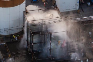 An aerial view of water being sprayed onto an overheated 34,000-gallon chemical tank with water vapor blurring details of the structures.