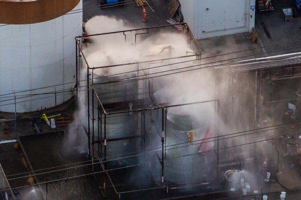 An aerial view of water being sprayed onto an overheated 34,000-gallon chemical tank with water vapor blurring details of the structures.