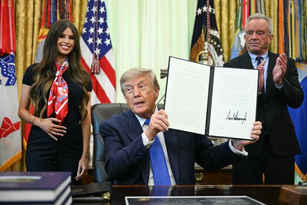 Donald Trump holds up an executive order with Robert F. Kennedy, Jr., and Jayme Leagh Franklin on either side.