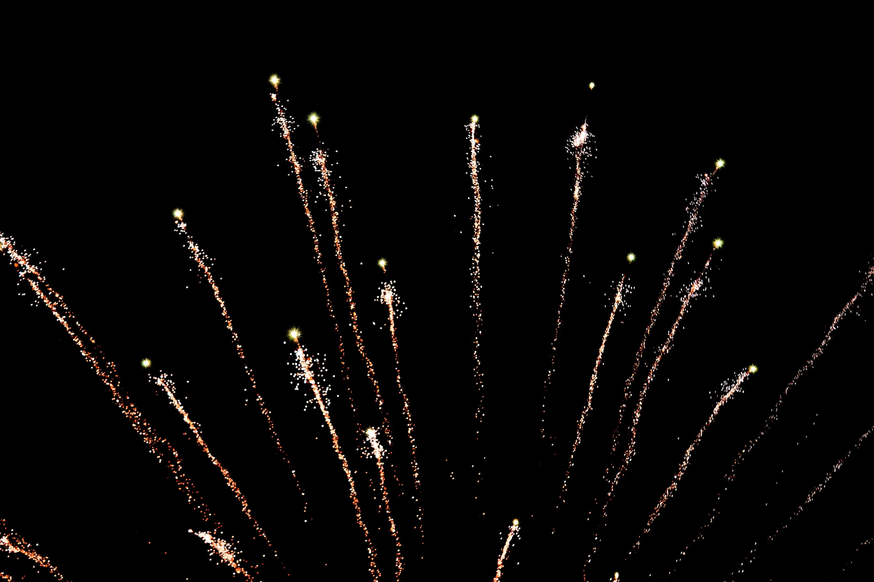 Several fireworks launch to different heights, trailing white sparks. They haven't burst yet.
