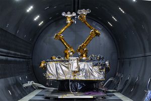 A silver foil-wrapped box bristling with electronic gadgets and two robotic arms sits in a cryogenic thermal vacuum chamber.