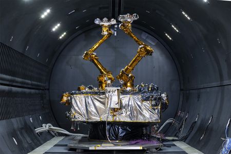 A silver foil-wrapped box bristling with electronic gadgets and two robotic arms sits in a cryogenic thermal vacuum chamber.