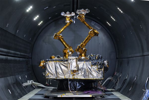 A silver foil-wrapped box bristling with electronic gadgets and two robotic arms sits in a cryogenic thermal vacuum chamber.