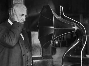 Thomas Edison stands next to a phonograph.