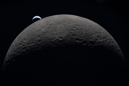 A crescent Earth sets behind the far side of the moon.
