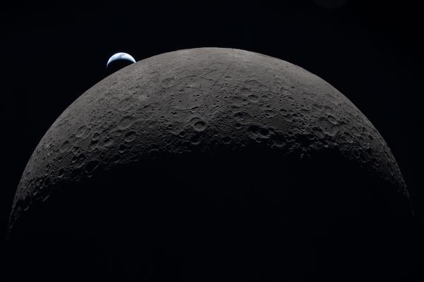 A crescent Earth sets behind the far side of the moon.