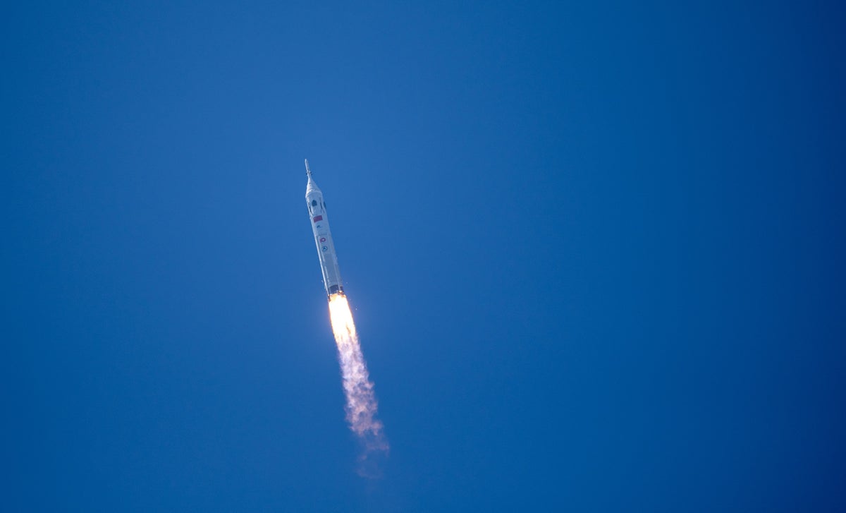 A Chinese Long March 10 rocket soars through a clear blue sky on a fiery exhaust plume