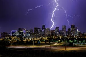 Bright lightning arcs through the night sky toward a city skyline.
