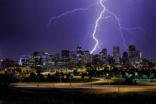 Bright lightning arcs through the night sky toward a city skyline.